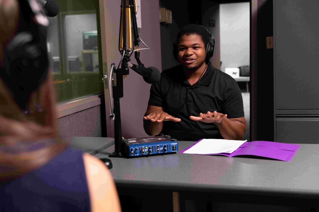 Zacchaeus smiles as he talks into a podcast microphone.