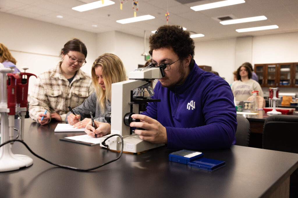 Jackson Scott sits at a table with other students. He's looking into a microscope.