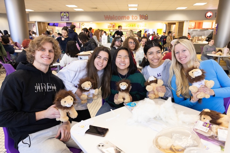 Sydney Castillo and four other students sit at a table in the Guillot University Center (GUC). They smile as they hold stuffed animal lions.
