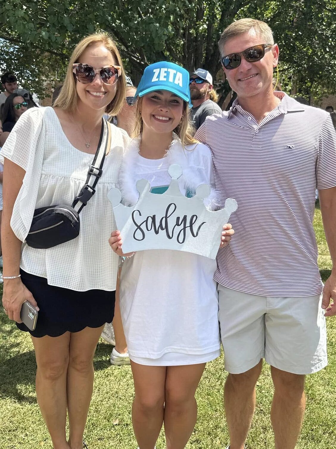 Sadye smiles and poses with her parents outside. 
