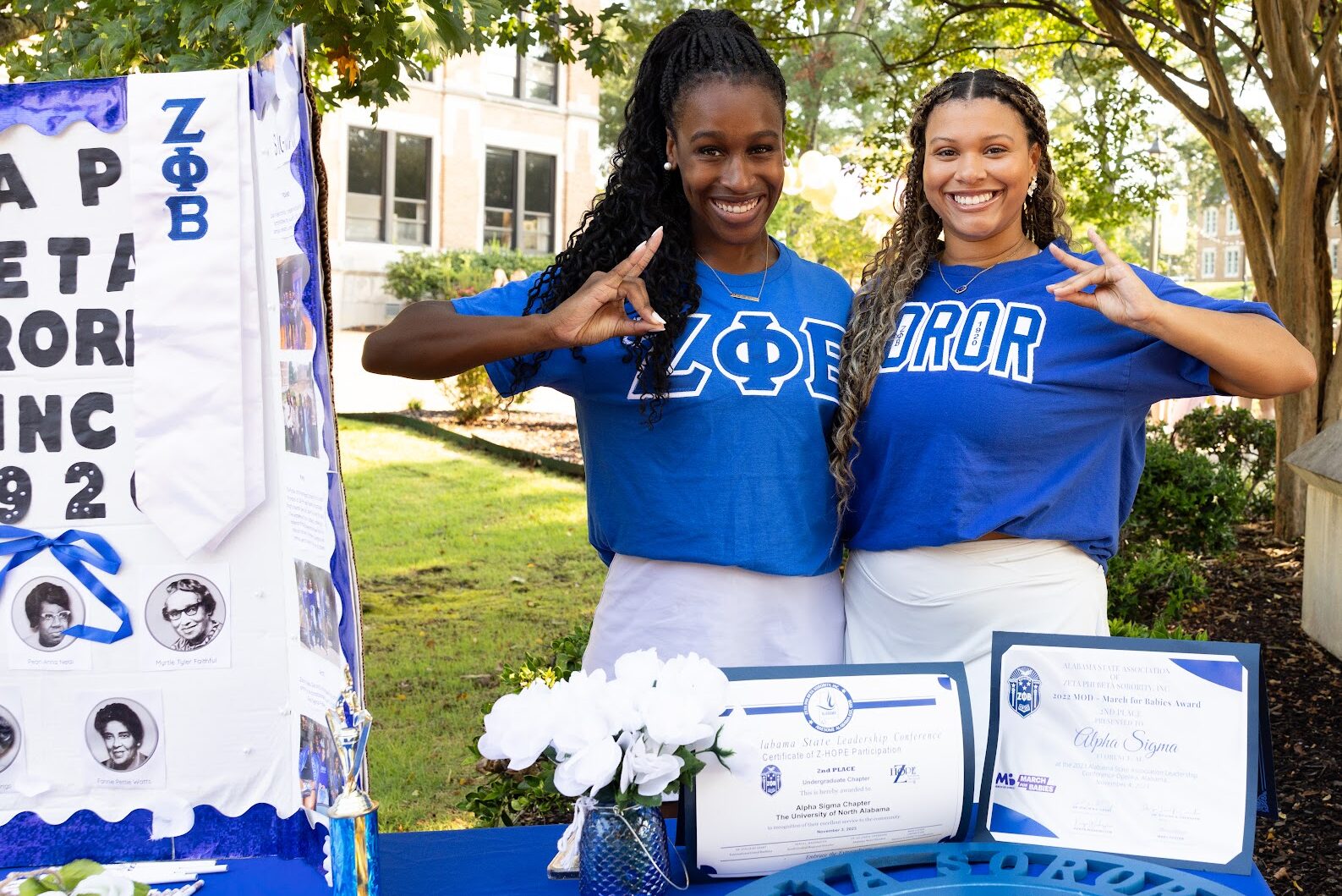 Krimsyn Jones and another ZOE Alpha Sigma NPHC member smile and pose at a table set up with sorority info.