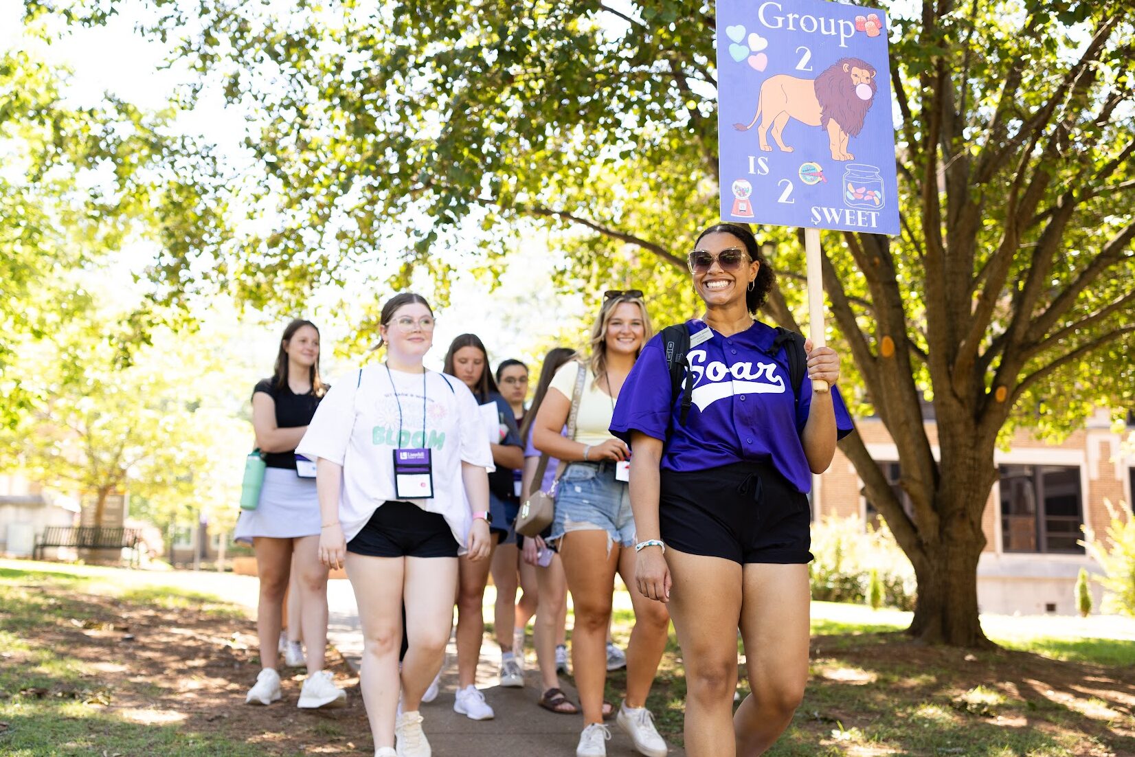 Krimsyn smiles for the camera as she leads future UNA students around campus for SOAR. She's holding up a sign that says, "Group 2 is 2 sweet."