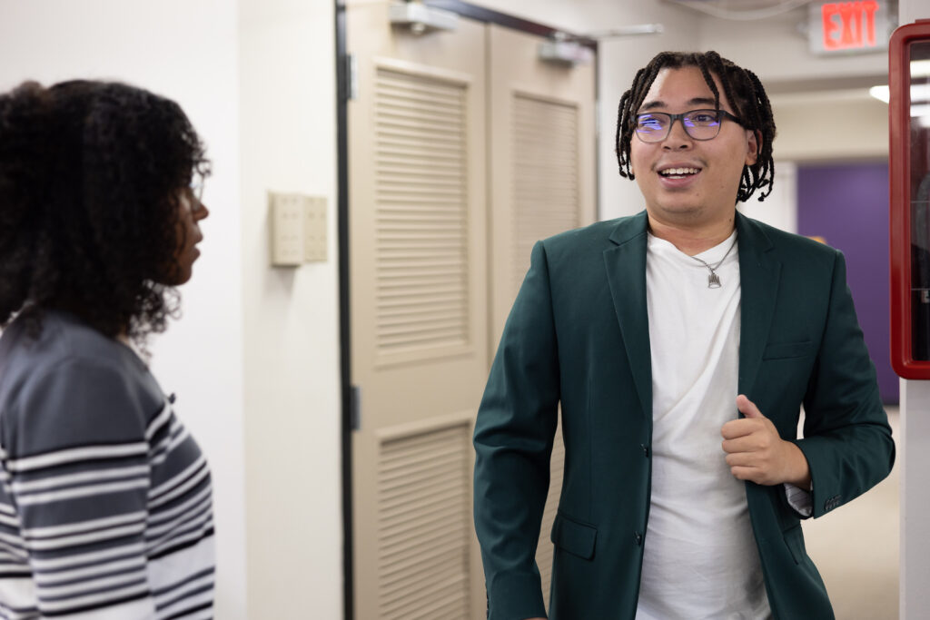 Micah Metcalf smiles as he stands in a UNA hallway talking to another student.