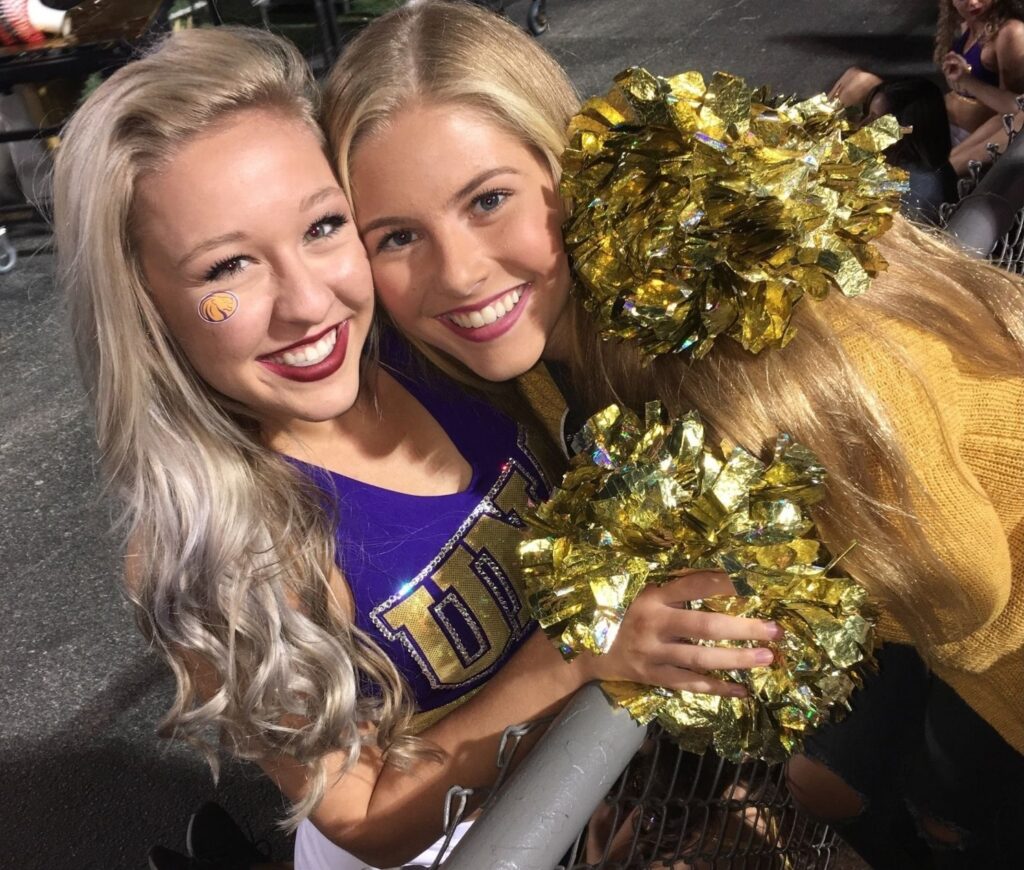 Allie Lopez and Haley Gilbertson (Miss UNA 2018) smile and pose for the photo. Haley is holding cheerleader pompoms.