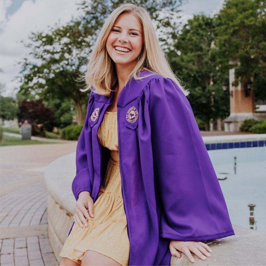 Allie smiles as she poses in her University of North Alabama graduation gown. She sits on the edge of Harrison Fountain.